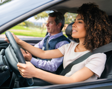 A cheerful girl behind the wheel with an instructor in a car